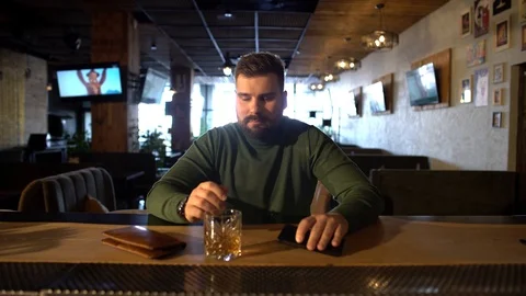 A bearded man at the bar drinks whiskey with ice Stock Footage 126030291