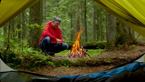 A bearded man basking near a fire in a beautiful forest Stock Footage 158759375