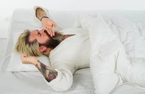 Bearded man in bathrobe lying on soft white pillow and yawning. Handsome man  Stock Photos