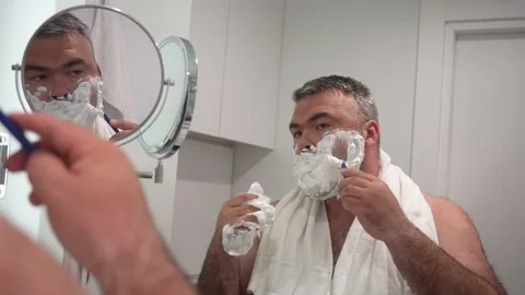 Bearded Man in bathroom. guy applies white foam shaving on cheeks Stock Footage 239760579