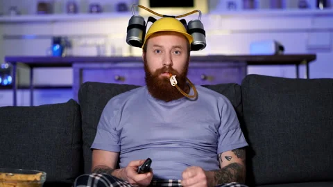 Bearded man with beea helmet sitting on the sofa at home, drinking beer. Stock Footage 122588305