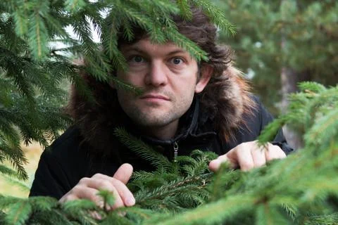 Bearded man with big round goggle eyes looking out of the forest through the Stock Photos