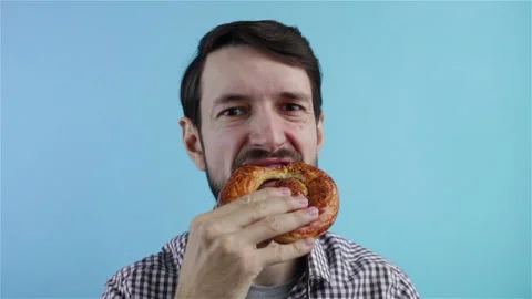 Bearded man biting and eating bretzel on blue background portrait shot Stock Footage 123063894