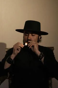 A bearded man in a black hat lights a cigar with a match Foto stock