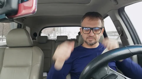 Bearded man in blue clothes wears glasses and starts drive car Stock Footage 124249608