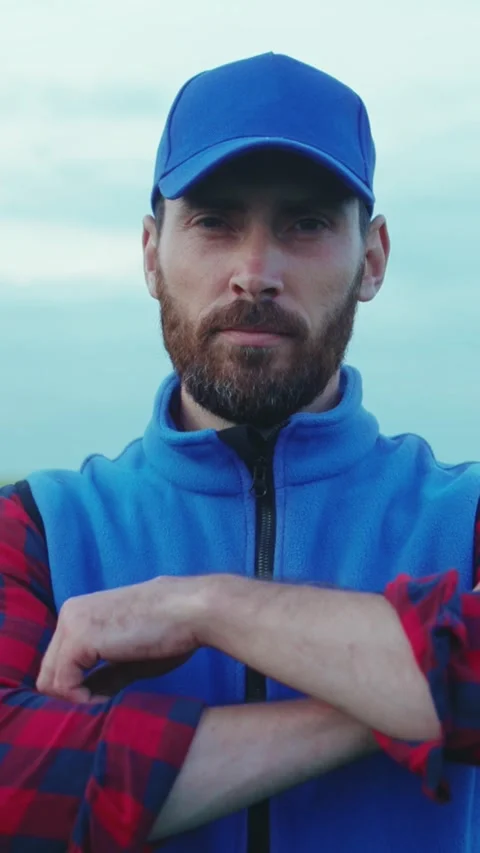 A bearded man in a blue hat and vest stands confidently in a field Stock Footage 305950186