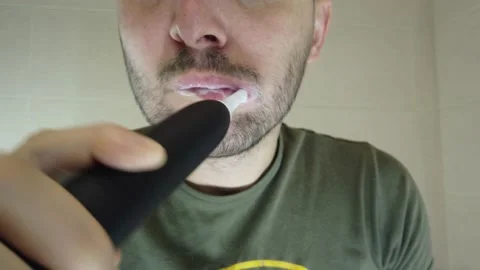 A bearded man brushes his teeth in the mirror with his mouth open. Stock Footage 144010323