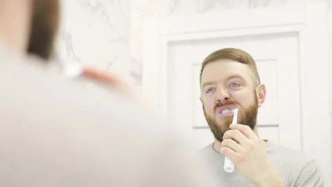 Bearded man brushes his teeth in front of mirror. Stock Footage 180404314