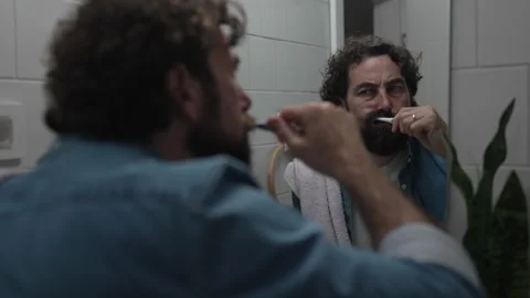 Bearded man brushing his teeth in bathroom mirror 스톡 동영상 336624727