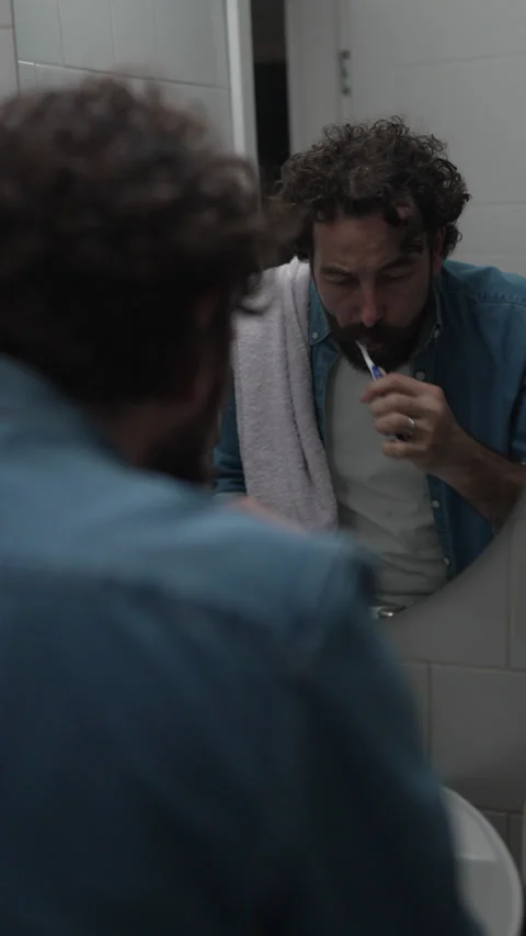 Bearded man brushing his teeth in bathroom mirror Vídeos de archivo 336624730