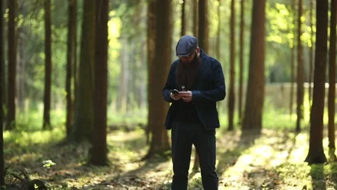 Bearded man in cap and glasses smokes an electronic cigarette and talks to phone Vídeos de archivo 110736182