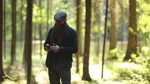 Bearded man in cap and glasses smokes an electronic cigarette and talks to phone Stock Footage 110736202