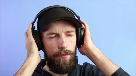 Bearded man in cap listen music in headphones and shaking head portrait shot Stock Footage 129502953