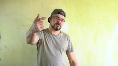 A bearded man in a cap stands against the wall and points a finger 4K Stock Footage 125283248