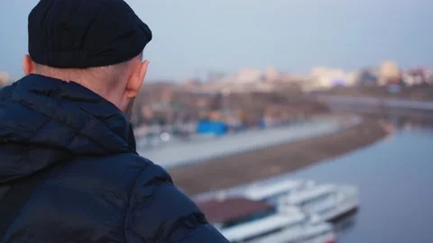 A bearded man in a cap. View from the back. Looks at the river from the bridge Stock Footage 153641118