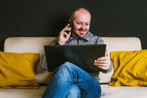 Bearded man in casual clothes using laptop on couch Stock Photos