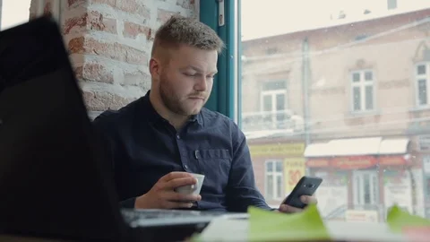 The bearded man checks email on a smartphone and drinks a cup of coffee in a 動画素材 90818904
