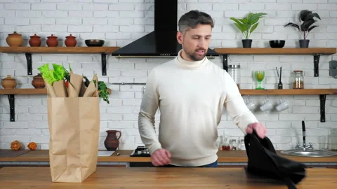 Bearded man chef in white sweater comes to home kitchen puts on black apron Stock Footage 149745830