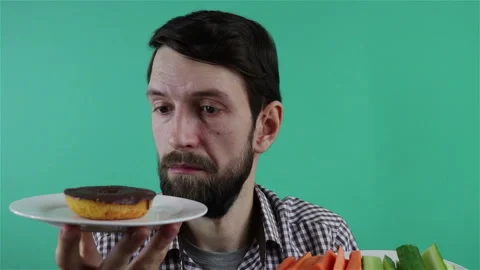 Bearded man choosing between the chocolate donut and carrot and cucumber sticks Stock Footage 124269063