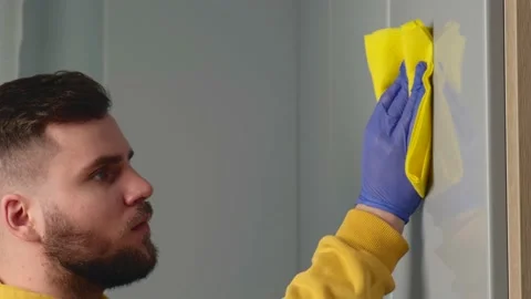 Bearded man cleaning the house using special gloves and wearing a yellow sweater Stock Footage 146582461