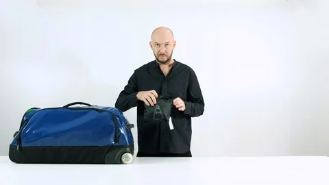 Bearded man collects things in a suitcase for travel. Blue bag Stock Footage 102788695