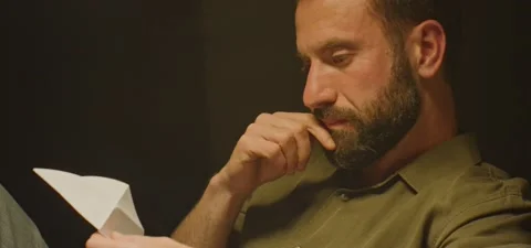Bearded man on couch thinking, creating a bird from paper, evening Stock Footage 201143661