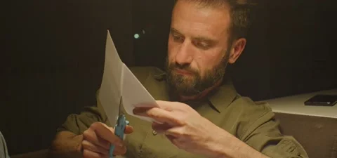 Bearded man on couch thinking, cutting paper, evening Stock Footage 201143516