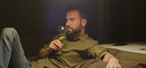Bearded man on couch thinking, drinking from glass, evening Stock Footage 201143645