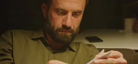 Bearded man on couch thinking, folding a bird from paper, evening Stock Footage 201143517