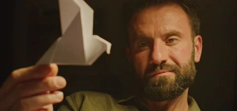 Bearded man on couch thinking, playing with paper bird, evening Stock Footage 201143720