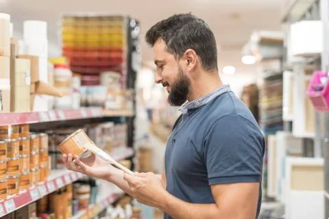 Bearded man in craft store selecting paint for work at home Stock Photos