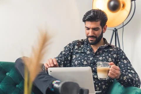 Bearded man with a cup of warm coffee is working with a help of tablet in the Stock Photos