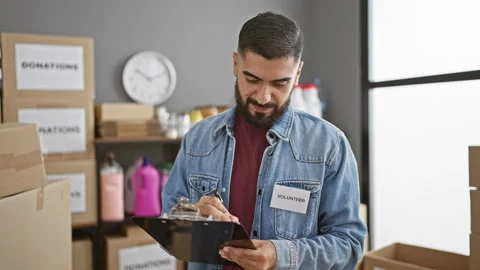A bearded man in a denim jacket and 'volunteer' badge writes on a clipboard.. Stock Footage 272161655