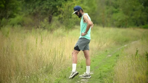 Bearded man doing high knee warm-up on grassy trail in summer meadow outside Stock Footage 313951494