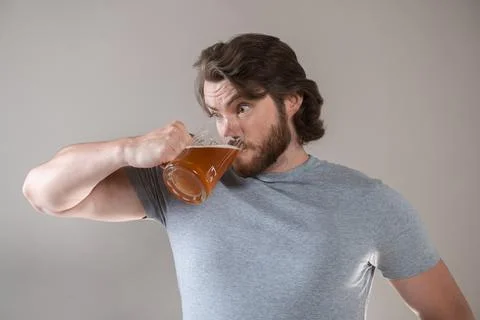 Bearded man drinking beer with a big mug on a gray background Stock Photos