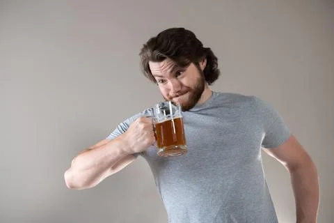 Bearded man drinking beer with a big mug on a gray background Stock Photos
