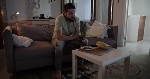Bearded man drinking beer on sofa and watching TV Stock Footage 271161542