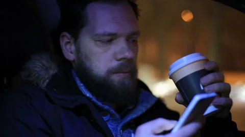 Bearded man drinking coffee and Uses the phone in the car. Stock Footage 87959267