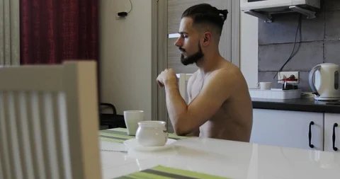 A bearded man is drinking coffee sitting at a table in the kitchen. Stock Footage 118774149