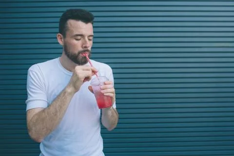 Bearded man is drinking lemonade from plastic cup through straw. He is holdin Stockfoto's