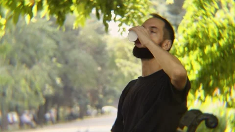 Bearded Man Drinking from Paper Cup Sitting on Bench in Park Video stock 342824604