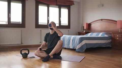Bearded man drinking water while resting on the floor from his home exercise.  Stock Footage 158488008