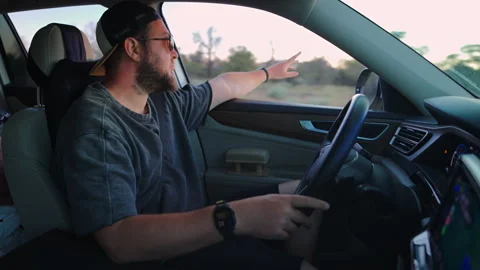 Bearded Man Driving Car and Pointing Out Window During Golden Hour Road Trip. Stock-Footage 342491678