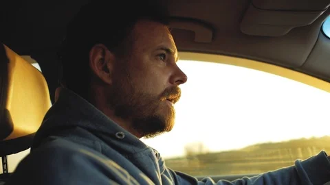 Bearded man driving a car on sunset background Stock Footage 103217695