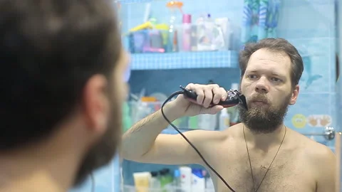 Bearded man dry shaving beard using electric trimmer machine Video stock 97245467