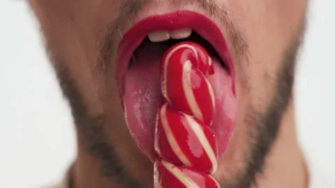 Bearded man eat candy, lick it with pleasure on white background close-up Stock Footage 147573932