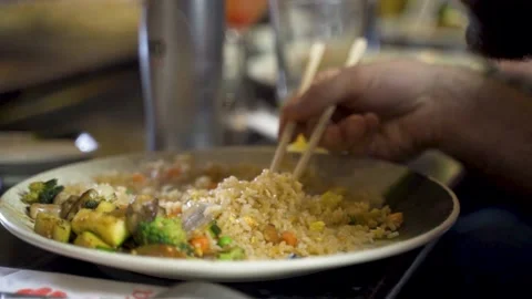 Bearded man eating fried rice with chop sticks at dinner table, slow motion Stock Footage