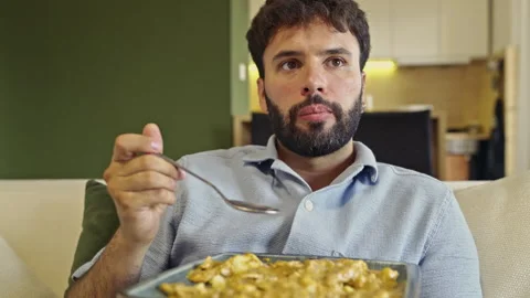 Bearded Man Eats a Casual Breakfast Cereal on the Couch While Watching TV, With Stock Footage 318833486