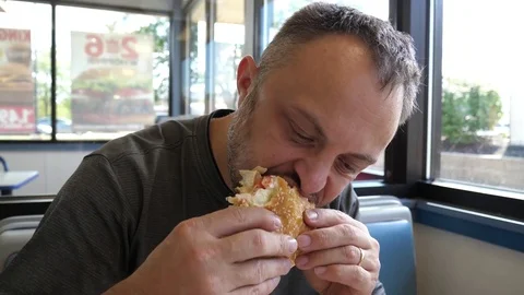 Bearded man eats hamburger burger sandwich at the fast food chain restaurant Stock Footage 80746389