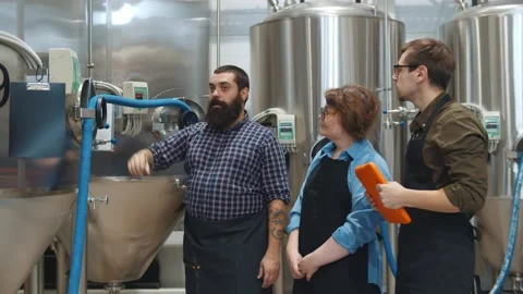 Bearded man engineer showing two apprentice beer tanks in large brewery 스톡 동영상 144538790